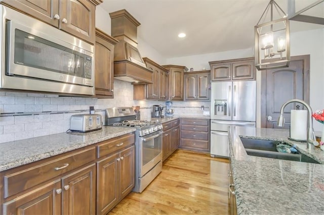 kitchen featuring sink, pendant lighting, stainless steel appliances, light stone countertops, and decorative backsplash