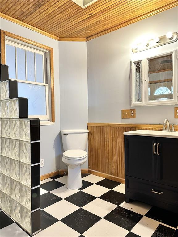 bathroom with toilet, wooden walls, wooden ceiling, crown molding, and vanity