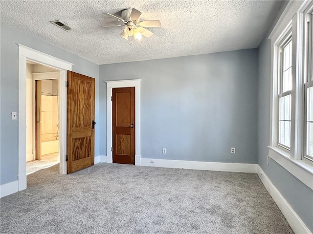 carpeted spare room with a textured ceiling, ceiling fan, and a healthy amount of sunlight