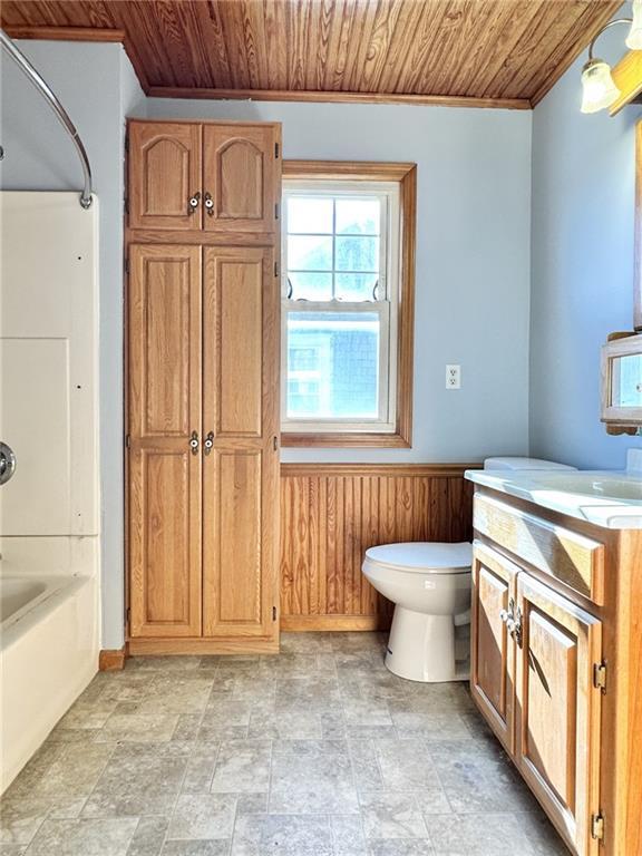 full bathroom with toilet, wooden ceiling, wooden walls, and vanity