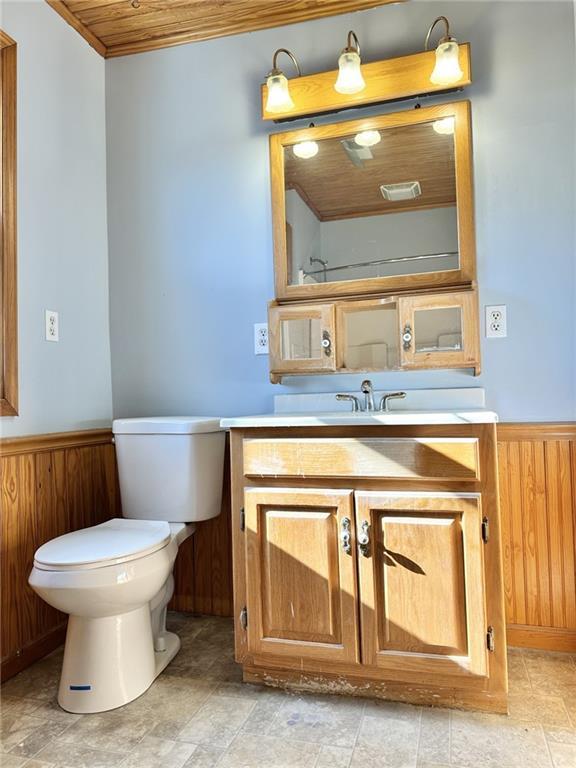 bathroom featuring toilet, wooden ceiling, wood walls, and vanity