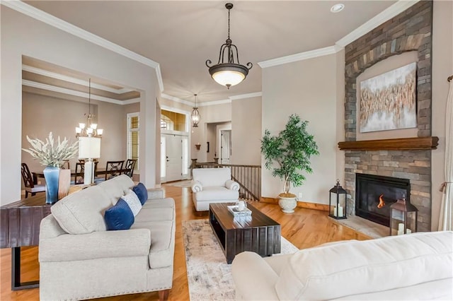 living room with a notable chandelier, crown molding, a stone fireplace, and light hardwood / wood-style floors