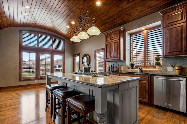 kitchen featuring a center island, hanging light fixtures, dark stone counters, stainless steel appliances, and light hardwood / wood-style floors