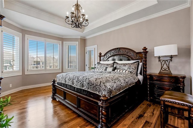 bedroom featuring crown molding, wood-type flooring, a tray ceiling, and an inviting chandelier