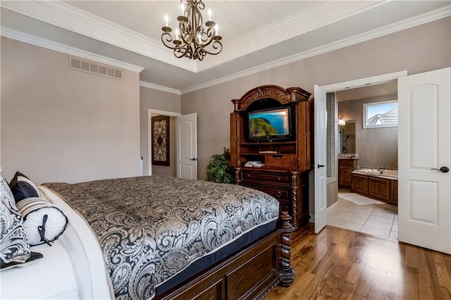 bedroom featuring ensuite bathroom, crown molding, a chandelier, light wood-type flooring, and a raised ceiling