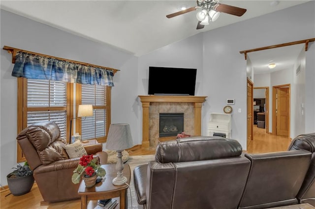 living room with vaulted ceiling, a tile fireplace, ceiling fan, and light wood-type flooring