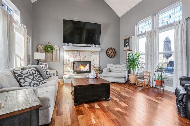 living room with hardwood / wood-style flooring, a stone fireplace, and high vaulted ceiling