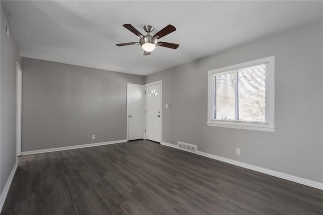 empty room featuring dark wood-type flooring, a ceiling fan, visible vents, and baseboards