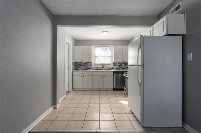 kitchen featuring visible vents, decorative backsplash, stainless steel dishwasher, freestanding refrigerator, and white cabinetry