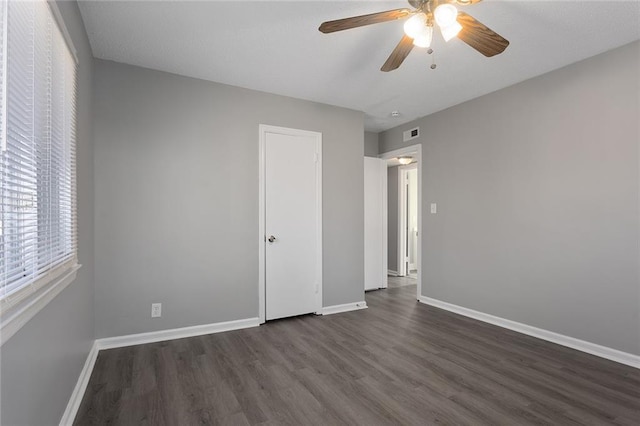 unfurnished bedroom with dark wood-style floors, ceiling fan, visible vents, and baseboards