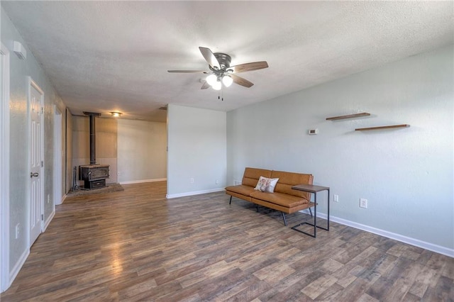 sitting room with a wood stove, ceiling fan, a textured ceiling, and wood finished floors