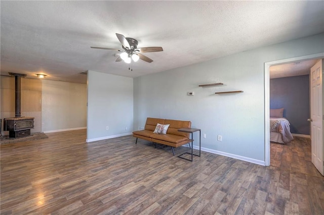 sitting room with a textured ceiling, wood finished floors, a wood stove, and a ceiling fan