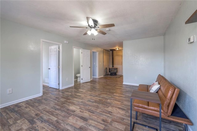 living area with ceiling fan, a textured ceiling, wood finished floors, baseboards, and a wood stove