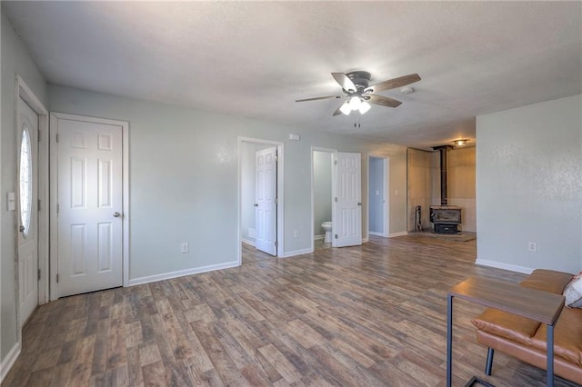 unfurnished living room featuring a ceiling fan, a wood stove, a textured ceiling, wood finished floors, and baseboards