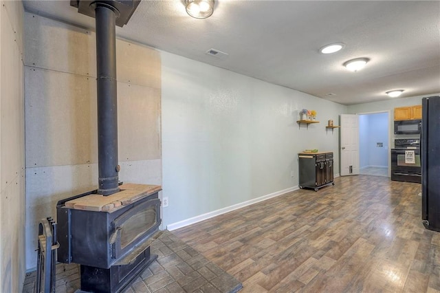 living room featuring a wood stove, visible vents, baseboards, and wood finished floors