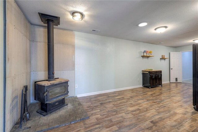 living room with baseboards, visible vents, wood finished floors, a wood stove, and a textured ceiling