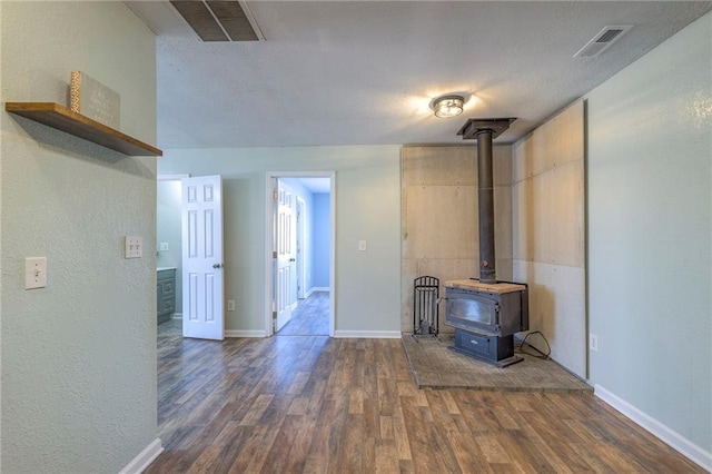 unfurnished living room with a wood stove, dark wood-type flooring, visible vents, and baseboards