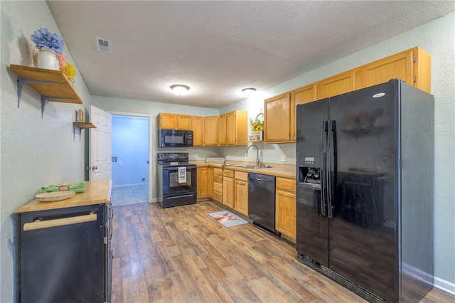 kitchen featuring black appliances, light wood finished floors, a sink, and visible vents