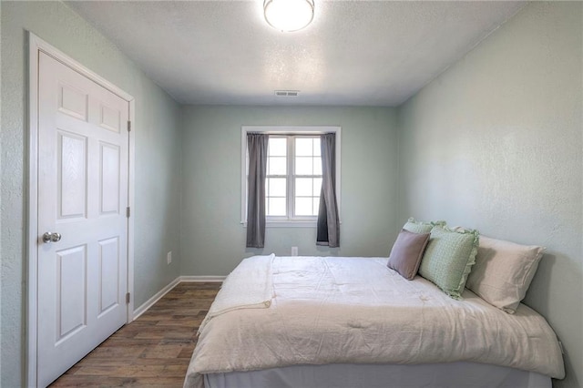 bedroom with dark wood-style floors, visible vents, a textured ceiling, and baseboards