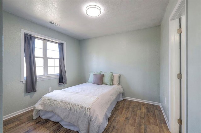 bedroom featuring baseboards, a textured ceiling, visible vents, and wood finished floors