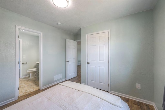 bedroom featuring wood finished floors, ensuite bath, visible vents, and baseboards