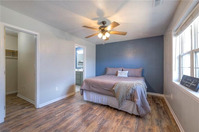 bedroom featuring visible vents, baseboards, a ceiling fan, ensuite bath, and wood finished floors