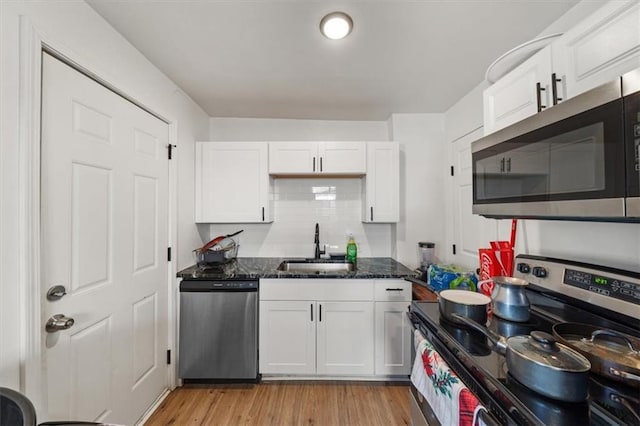 kitchen with stainless steel appliances, white cabinets, a sink, dark stone countertops, and light wood-type flooring