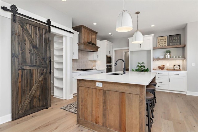 kitchen with white cabinets, an island with sink, sink, backsplash, and a barn door