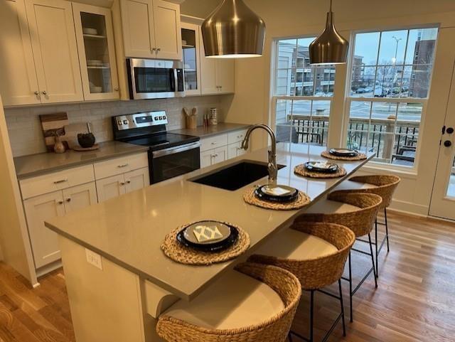 kitchen with sink, white cabinets, decorative backsplash, stainless steel appliances, and light hardwood / wood-style flooring