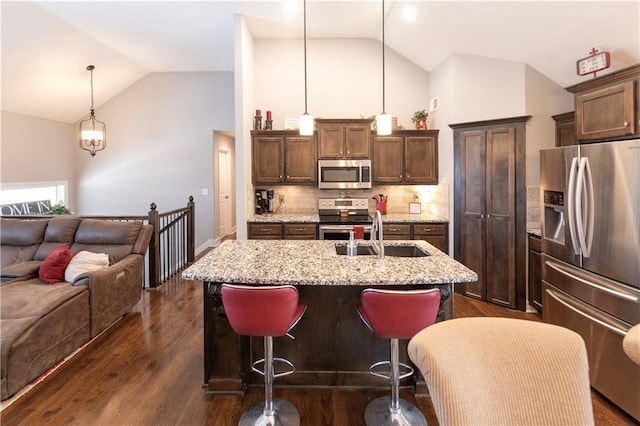 kitchen featuring stainless steel appliances, sink, backsplash, hanging light fixtures, and a center island with sink