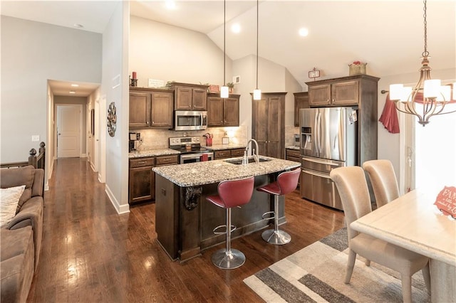 kitchen featuring appliances with stainless steel finishes, decorative light fixtures, a kitchen bar, tasteful backsplash, and sink