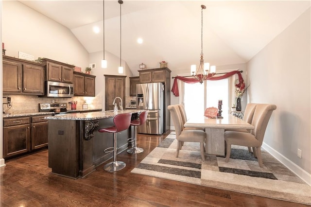 kitchen featuring hanging light fixtures, decorative backsplash, appliances with stainless steel finishes, and a center island with sink