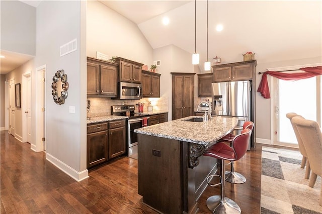 kitchen with a kitchen bar, sink, appliances with stainless steel finishes, an island with sink, and light stone counters