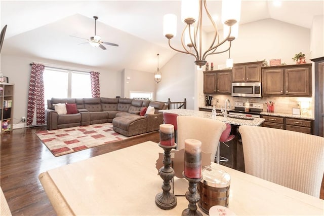 dining area featuring vaulted ceiling, dark wood-type flooring, sink, and ceiling fan with notable chandelier