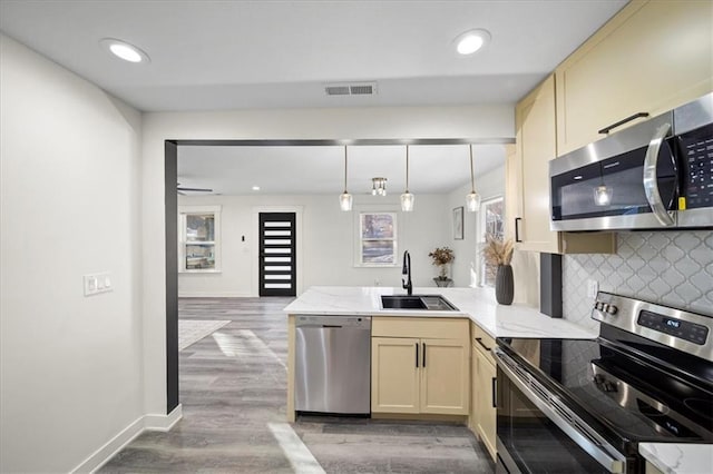 kitchen with appliances with stainless steel finishes, pendant lighting, sink, backsplash, and light hardwood / wood-style floors