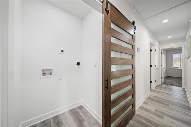 interior space featuring a barn door, electric dryer hookup, hookup for a washing machine, and light hardwood / wood-style floors