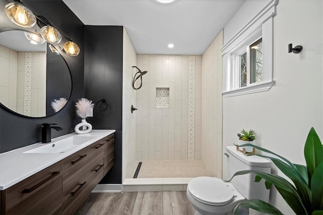 bathroom featuring a tile shower, vanity, wood-type flooring, and toilet