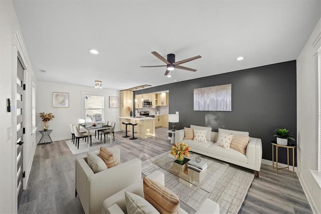 living room with ceiling fan, sink, and light wood-type flooring