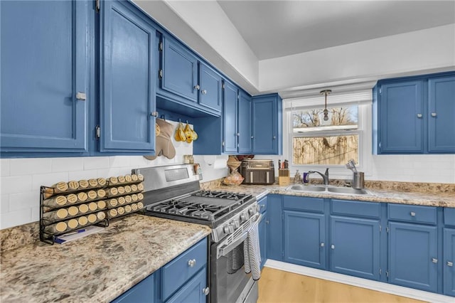 kitchen with sink, blue cabinetry, light stone counters, stainless steel gas range oven, and decorative light fixtures