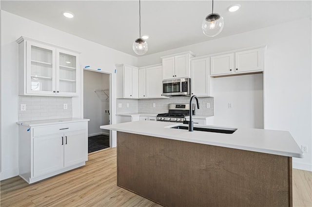 kitchen featuring white cabinets, decorative light fixtures, stainless steel appliances, sink, and a center island with sink