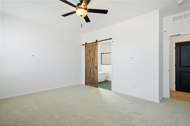 unfurnished room with ceiling fan, a barn door, and carpet flooring