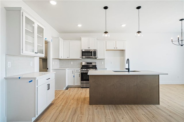 kitchen with appliances with stainless steel finishes, decorative light fixtures, white cabinetry, light hardwood / wood-style floors, and sink