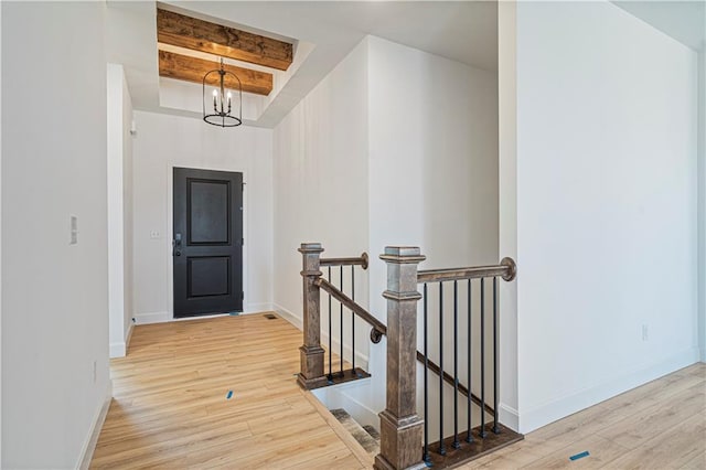 hallway featuring a notable chandelier, beamed ceiling, and light wood-type flooring