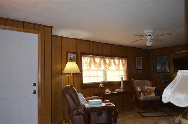 sitting room featuring ceiling fan, carpet, and wooden walls