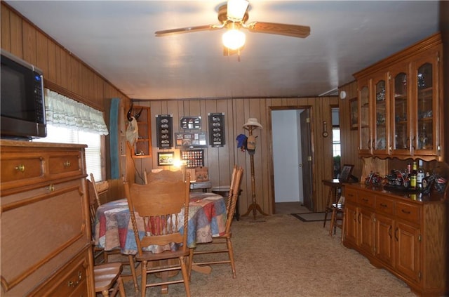 carpeted dining room featuring ceiling fan and wooden walls