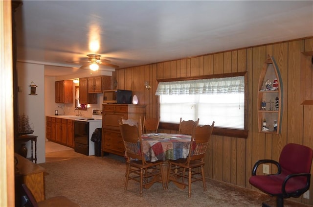 dining room with ceiling fan, light colored carpet, wood walls, and sink