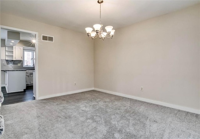 empty room featuring baseboards, visible vents, dark carpet, and a notable chandelier