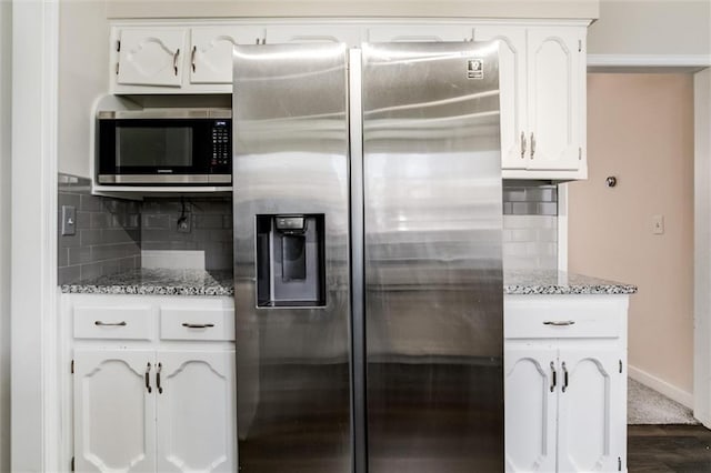 kitchen featuring baseboards, decorative backsplash, appliances with stainless steel finishes, light stone counters, and white cabinetry