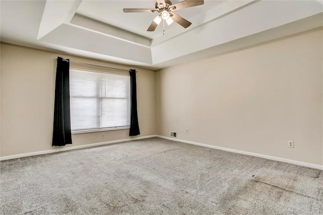 carpeted empty room with visible vents, baseboards, a raised ceiling, and a ceiling fan