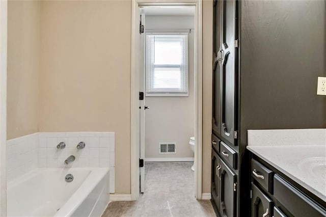 bathroom with toilet, vanity, baseboards, visible vents, and a bath